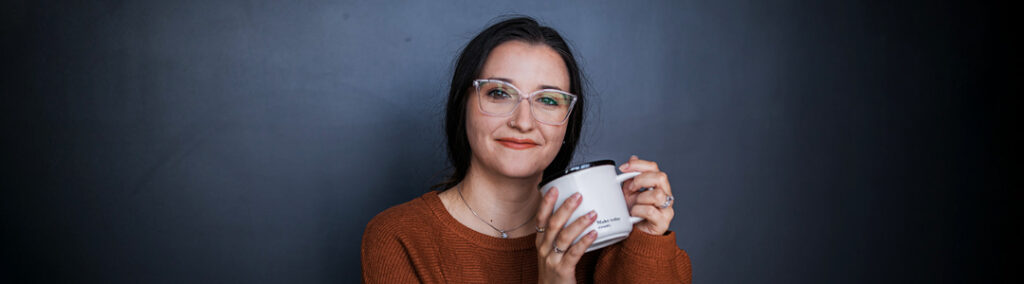 Tayshas Design Studio smiling at camera while holding coffee for stress management.