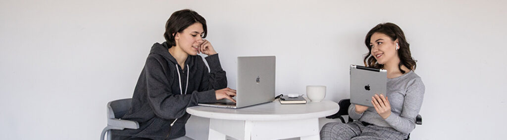 Two woman sitting at the same table typing on laptops crafting how to connect with your audience.