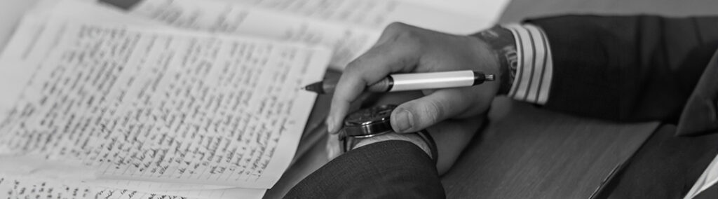 A stack of papers with handwriting filling the pages sitting on top of a desk. Hands crossed holding a pen that planned SEO optimization. 