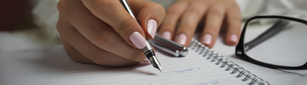 A hand holding a pen writing in an open journal stating "optimize your brand message with tayshas design studio."