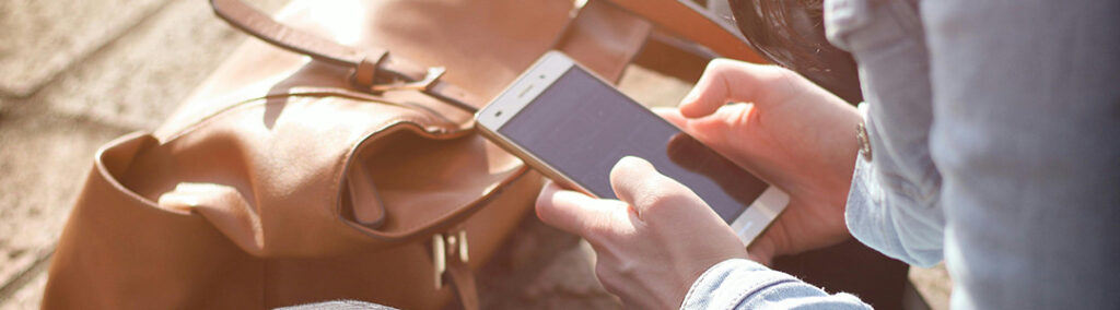 Someone holding a cell phone scrolling through their social media marketing next to a tan leather bag.