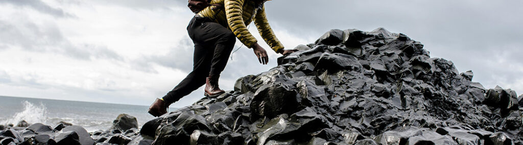 Someone climbing a stack of sharp, wet rocks next to the ocean to represent conquering challenges of social media marketing.