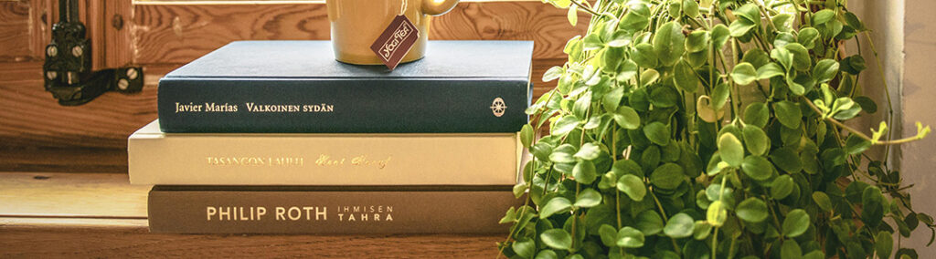 A stack of books sitting on a window seal next to a plant envisioning story telling.