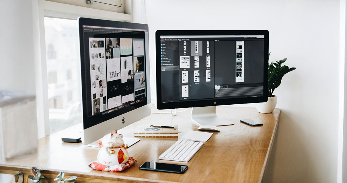 An office desk with two computer monitors that are designing a website.