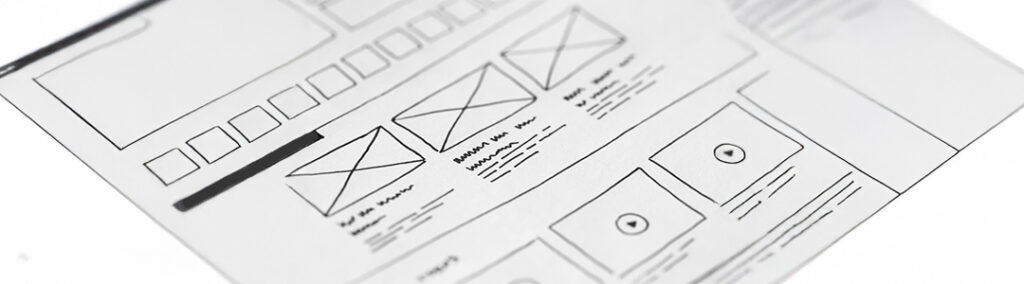 A website design wireframe drawn out on a piece of white paper and black pen.