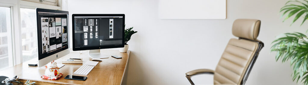 A wide shot of an office with two monitors that have website design open.